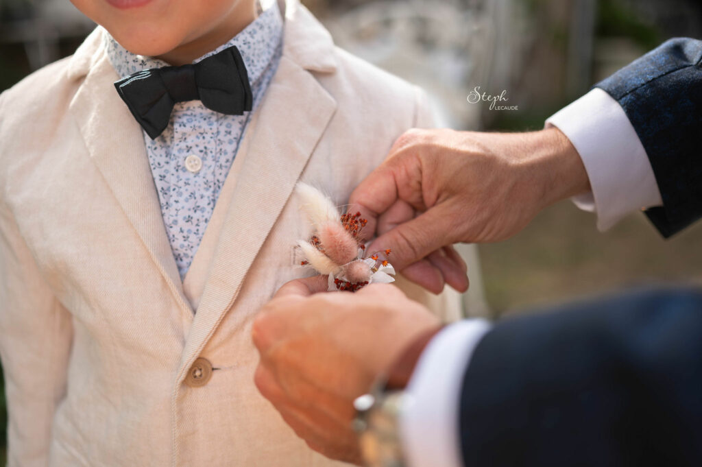 Inspiration_mariage_f&p_stephlecaude_20250823_0740 le marié aide le garçon d'honneur à installer sa broche fleural